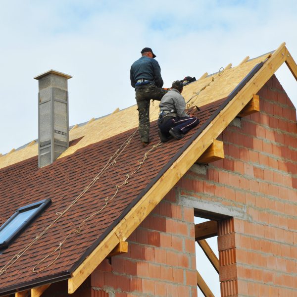 Roofing Construction and Building New Brick House with Modular Chimney, Skylights, Attic, Dormers and Eaves Exterior. Roofers Install, Repair Asphalt Shingles or Bitumen Tiles on the Rooftop Outdoor.